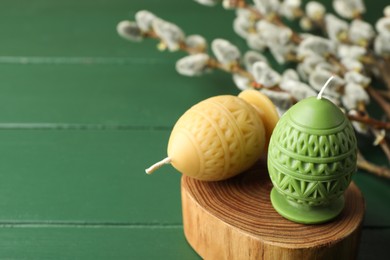 Photo of Colorful egg-shaped candles and willow branches on green table, closeup with space for text. Easter decor