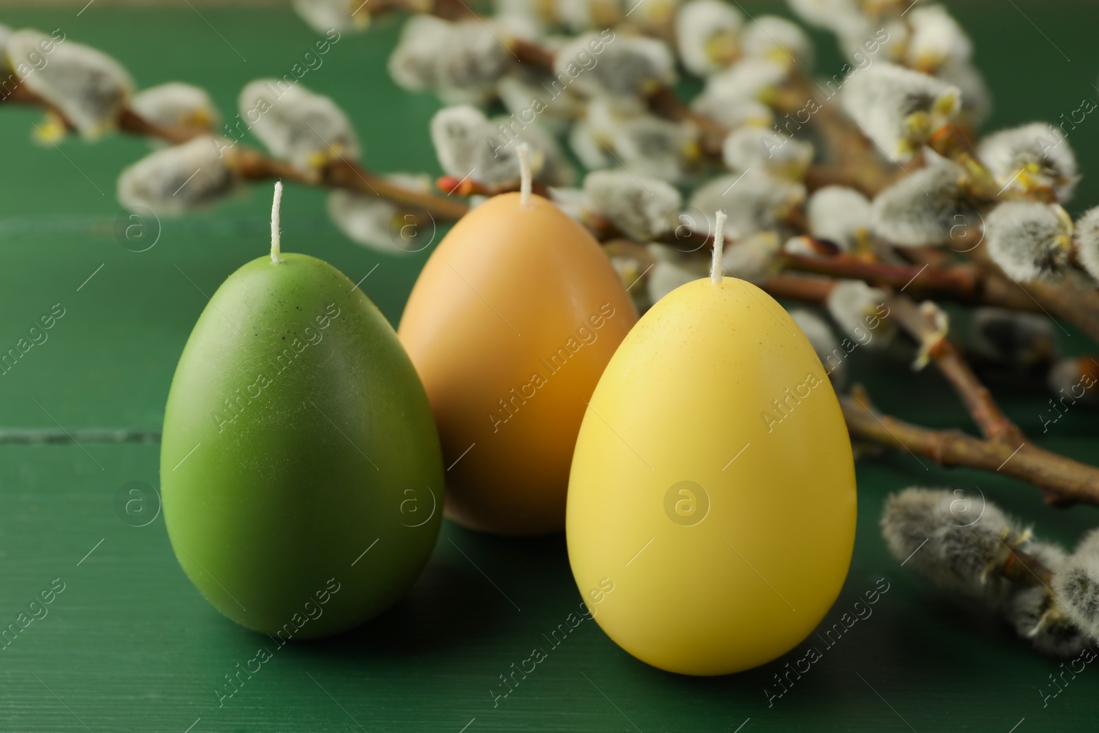 Photo of Colorful egg-shaped candles and willow branches on green wooden table, closeup. Easter decor