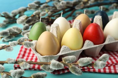 Photo of Colorful egg-shaped candles in carton on turquoise table, closeup. Easter decor