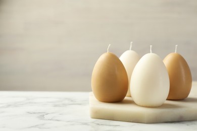 Photo of Egg-shaped candles on white marble table against light gray background, space for text. Easter decor