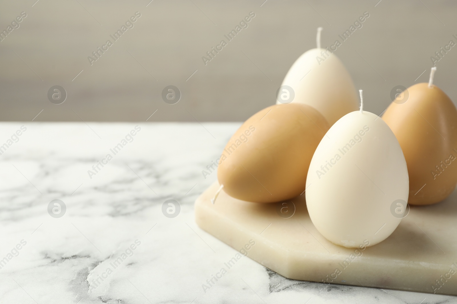 Photo of Egg-shaped candles on white marble table against light gray background, closeup and space for text. Easter decor