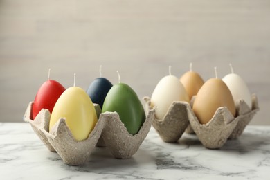 Photo of Colorful egg-shaped candles on white marble table against light gray background. Easter decor