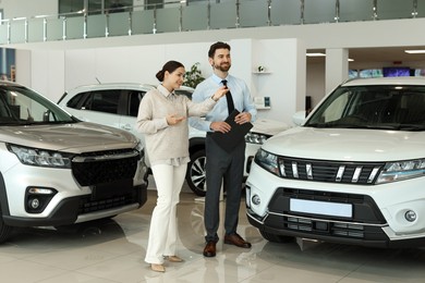 Happy salesman and client near new car in salon