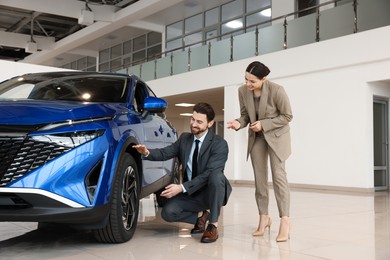 Photo of Happy saleswoman showing new blue car to client in salon