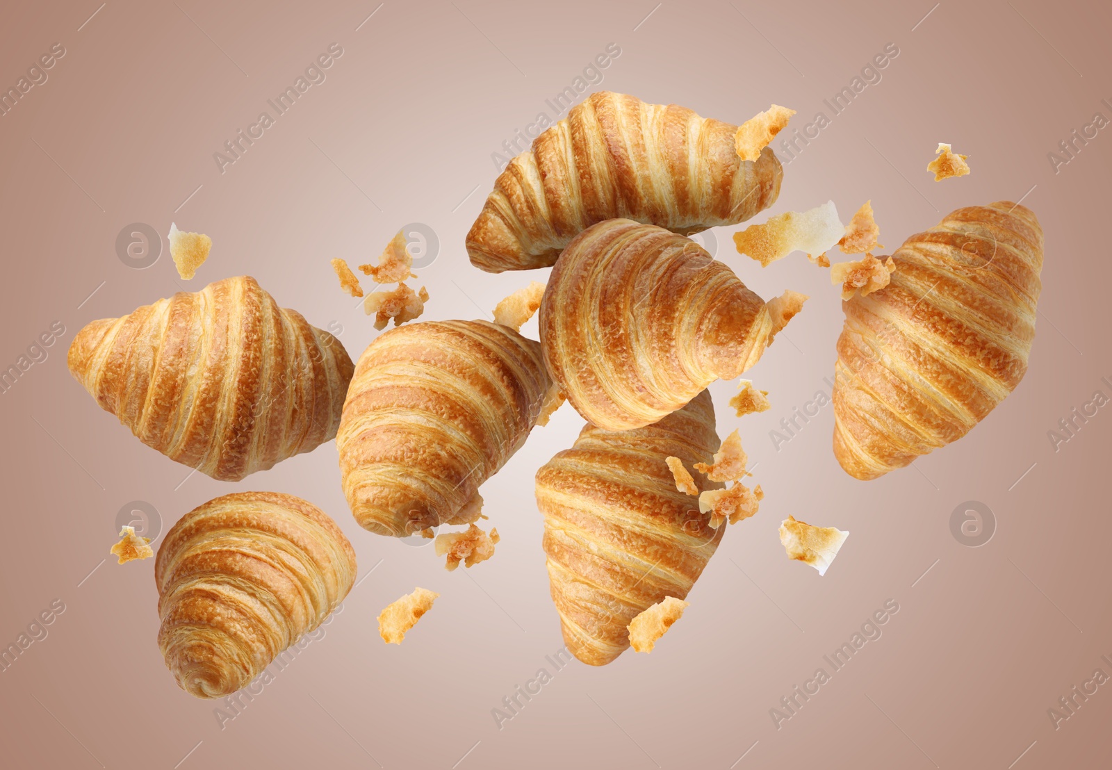 Image of Delicious croissants and crumbs in air on pale brown background. Puff pastry