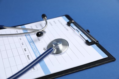 Photo of Stethoscope and medical card form on blue background, closeup