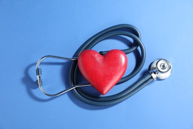 Photo of Stethoscope and red decorative heart on blue background, top view