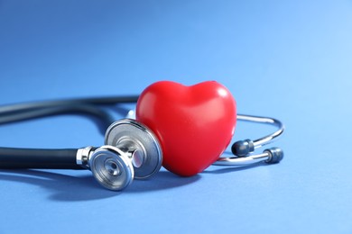 Photo of Stethoscope and red decorative heart on blue background, closeup