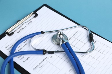 Photo of Stethoscope and medical card form on light blue background, closeup