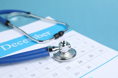 Photo of Stethoscope and calendar on light blue background, closeup
