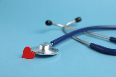 Photo of Stethoscope and red decorative heart on light blue background, closeup