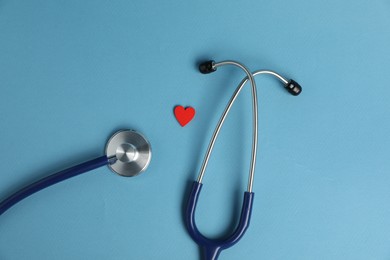 Photo of Stethoscope and red decorative heart on light blue background, flat lay