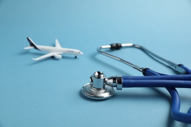 Photo of Stethoscope and airplane model on light blue background, closeup