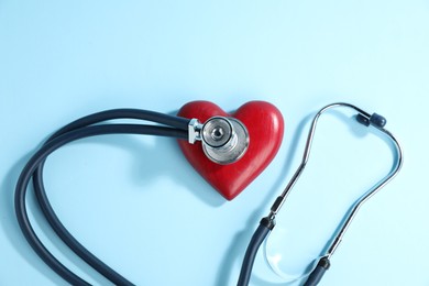 Photo of Stethoscope and red decorative heart on light blue background, top view
