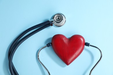 Photo of Stethoscope and red decorative heart on light blue background, top view