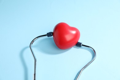 Photo of Stethoscope and red decorative heart on light blue background, top view