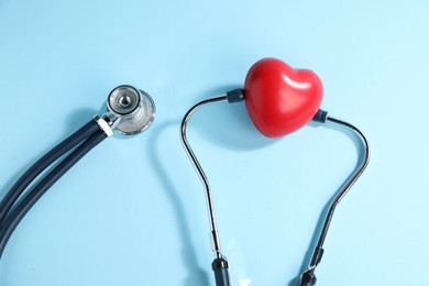 Photo of Stethoscope and red decorative heart on light blue background, top view