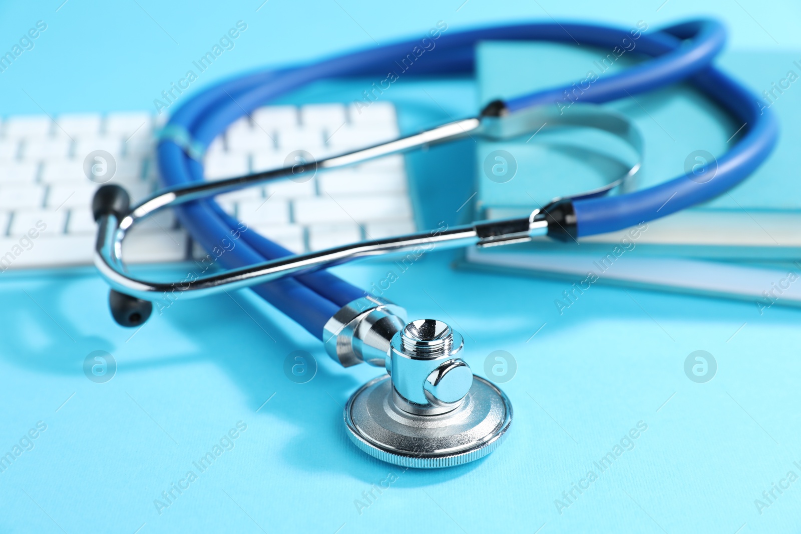 Stethoscope, keyboard and books on light blue background, closeup Photo of Stethoscope, keyboard and books on light blue background, closeup