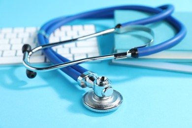 Photo of Stethoscope, keyboard and books on light blue background, closeup