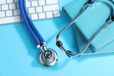 Photo of Stethoscope, keyboard and books on light blue background, flat lay