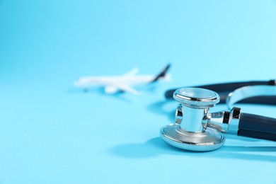 Photo of Stethoscope and airplane model on light blue background, selective focus. Space for text