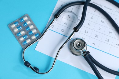 Photo of Stethoscope, calendar and pills on light blue background, flat lay