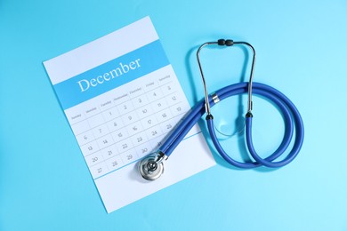 Photo of Stethoscope and calendar on light blue background, top view