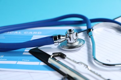 Photo of Stethoscope and medical card forms on light blue background, closeup