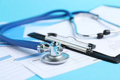Photo of Stethoscope and medical card forms on light blue background, closeup
