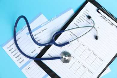 Photo of Stethoscope and medical card forms on light blue background, top view