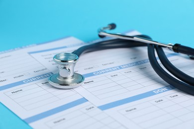 Photo of Stethoscope and medical card forms on light blue background, closeup