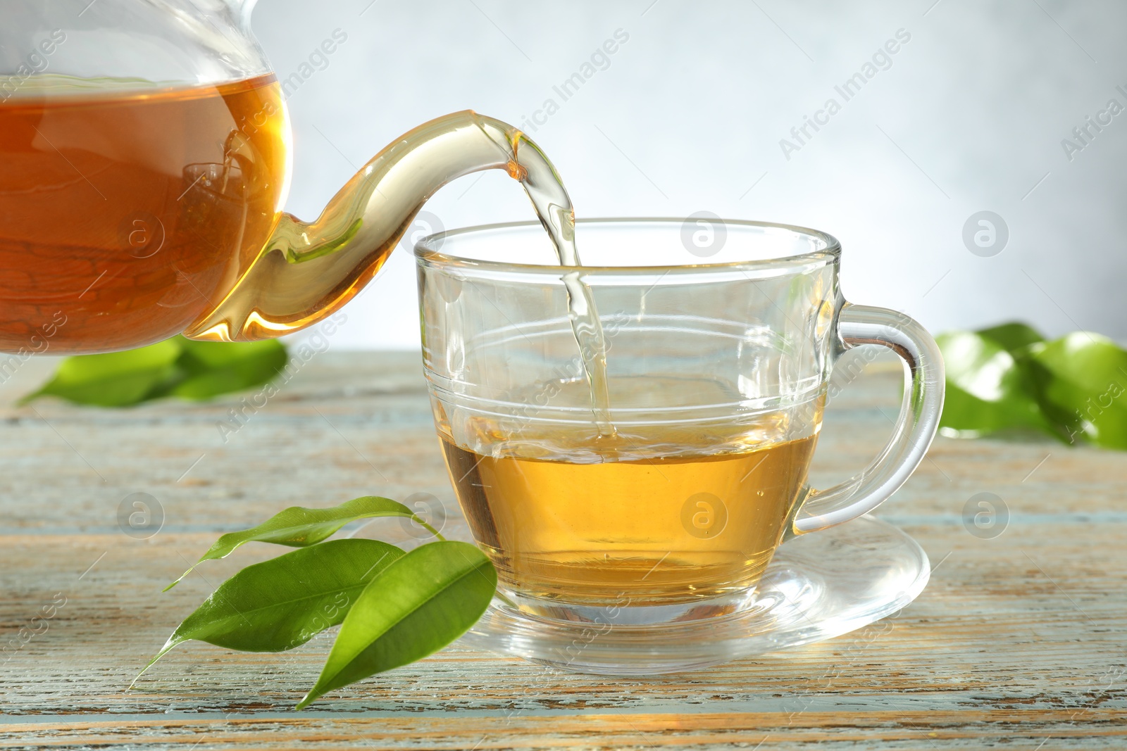 Pouring freshly brewed tea from teapot into glass cup on wooden table, closeup Photo of Pouring freshly brewed tea from teapot into glass cup on wooden table, closeup