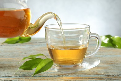 Photo of Pouring freshly brewed tea from teapot into glass cup on wooden table, closeup