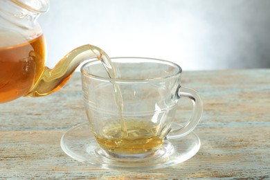 Photo of Pouring freshly brewed tea from teapot into glass cup on wooden table, closeup