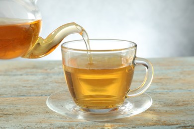 Photo of Pouring freshly brewed tea from teapot into glass cup on wooden table, closeup