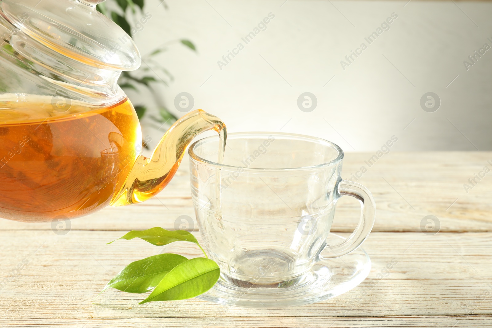 Pouring freshly brewed tea from teapot into glass cup on wooden table, closeup Photo of Pouring freshly brewed tea from teapot into glass cup on wooden table, closeup