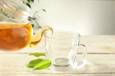 Photo of Pouring freshly brewed tea from teapot into glass cup on wooden table, closeup