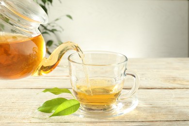 Photo of Pouring freshly brewed tea from teapot into glass cup on wooden table, closeup
