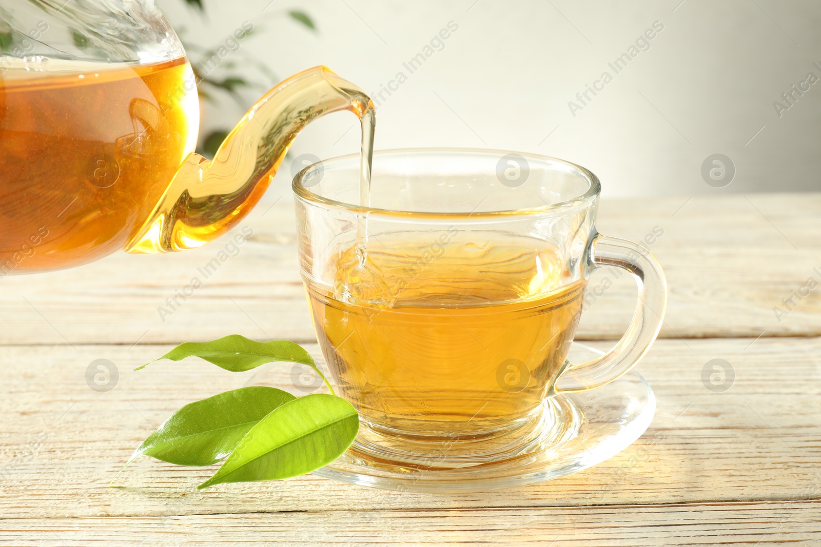 Pouring freshly brewed tea from teapot into glass cup on wooden table, closeup Photo of Pouring freshly brewed tea from teapot into glass cup on wooden table, closeup
