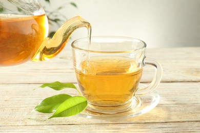 Photo of Pouring freshly brewed tea from teapot into glass cup on wooden table, closeup