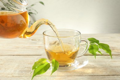 Photo of Pouring freshly brewed tea from teapot into glass cup on wooden table, closeup