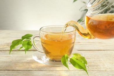 Photo of Pouring freshly brewed tea from teapot into glass cup on wooden table, closeup