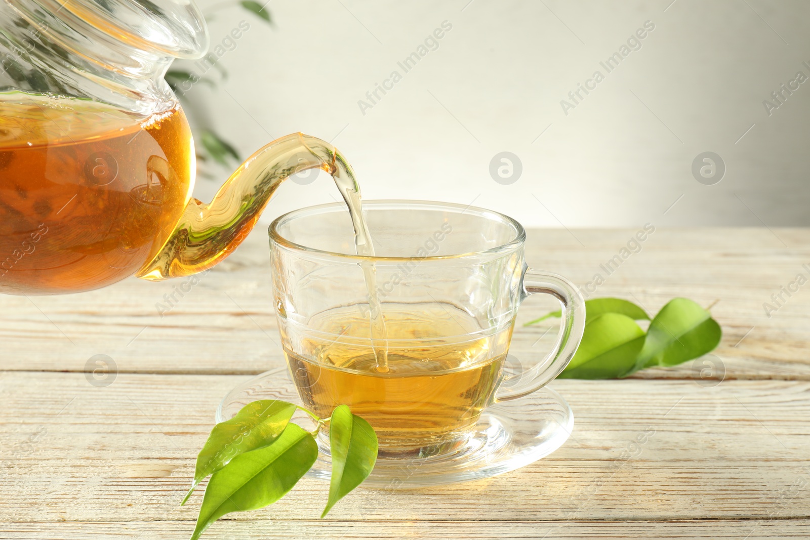 Pouring freshly brewed tea from teapot into glass cup on wooden table, closeup Photo of Pouring freshly brewed tea from teapot into glass cup on wooden table, closeup