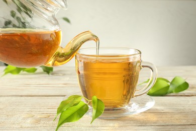 Photo of Pouring freshly brewed tea from teapot into glass cup on wooden table, closeup