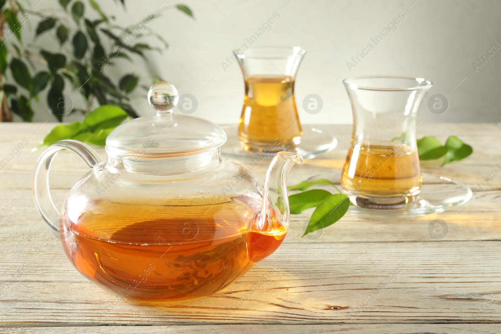 Freshly brewed tea in glass cups and teapot on wooden table Photo of Freshly brewed tea in glass cups and teapot on wooden table