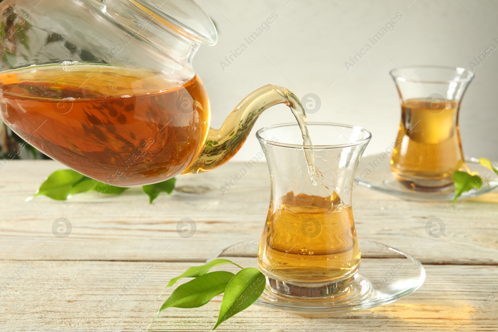 Pouring freshly brewed tea from teapot into glass cup on wooden table, closeup Photo of Pouring freshly brewed tea from teapot into glass cup on wooden table, closeup