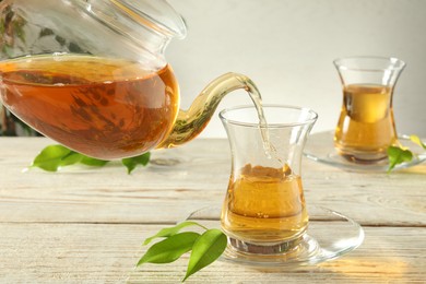 Photo of Pouring freshly brewed tea from teapot into glass cup on wooden table, closeup