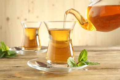 Photo of Pouring freshly brewed tea from teapot into glass cup on wooden table, closeup