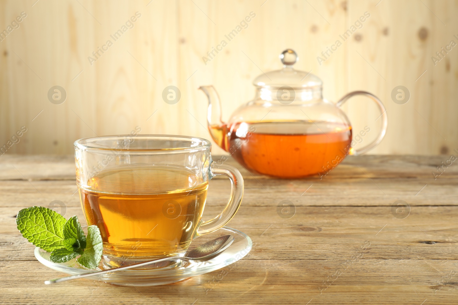Freshly brewed tea in glass cup and teapot on wooden table Photo of Freshly brewed tea in glass cup and teapot on wooden table