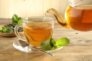 Photo of Pouring freshly brewed tea from teapot into glass cup on wooden table, closeup